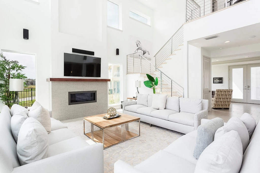 Sala de pé-direito alto, com sofás brancos e escada aberta, em casa do Reunion Village
