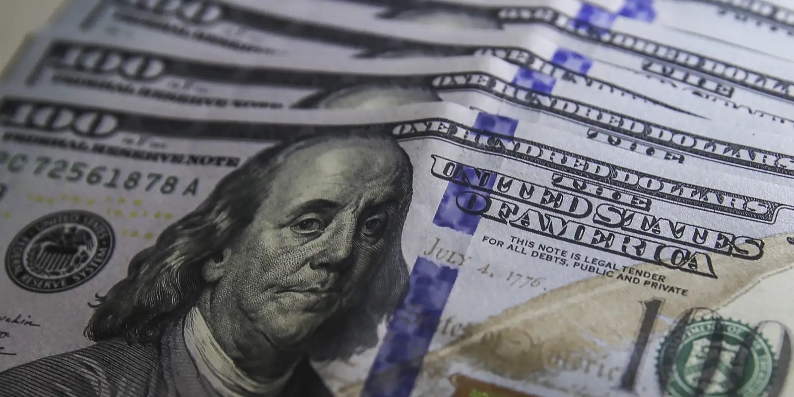 Cédulas de 100 dólares americanos em close, com o retrato de Benjamin Franklin
