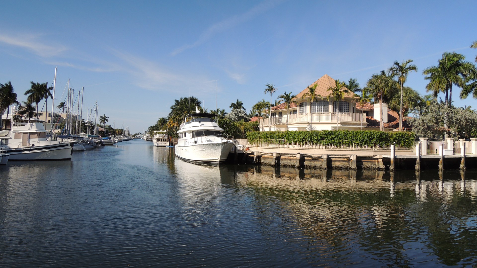Canal residencial em Fort Lauderdale, na Flórida, com iates e veleiros atracados e uma casa de telhado de cobre com cais próprio entre palmeiras