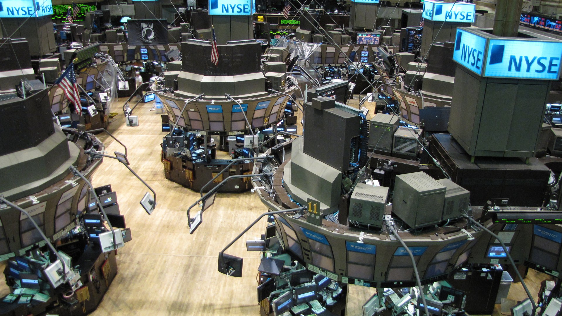 Salão de negociação da Bolsa de Nova York visto do alto, com os postos de operação cercados de monitores e os painéis azuis com a sigla NYSE