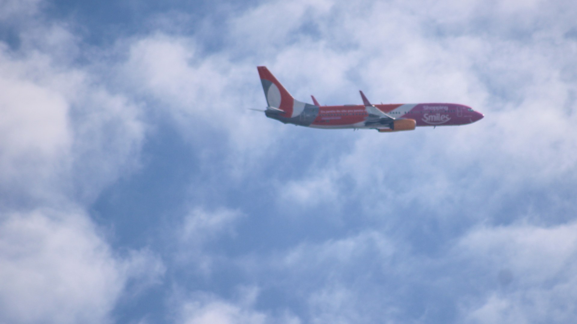 Boeing 737 da Gol, pintado de laranja, cinza e roxo com a marca Smiles, voando entre nuvens no céu de São Paulo