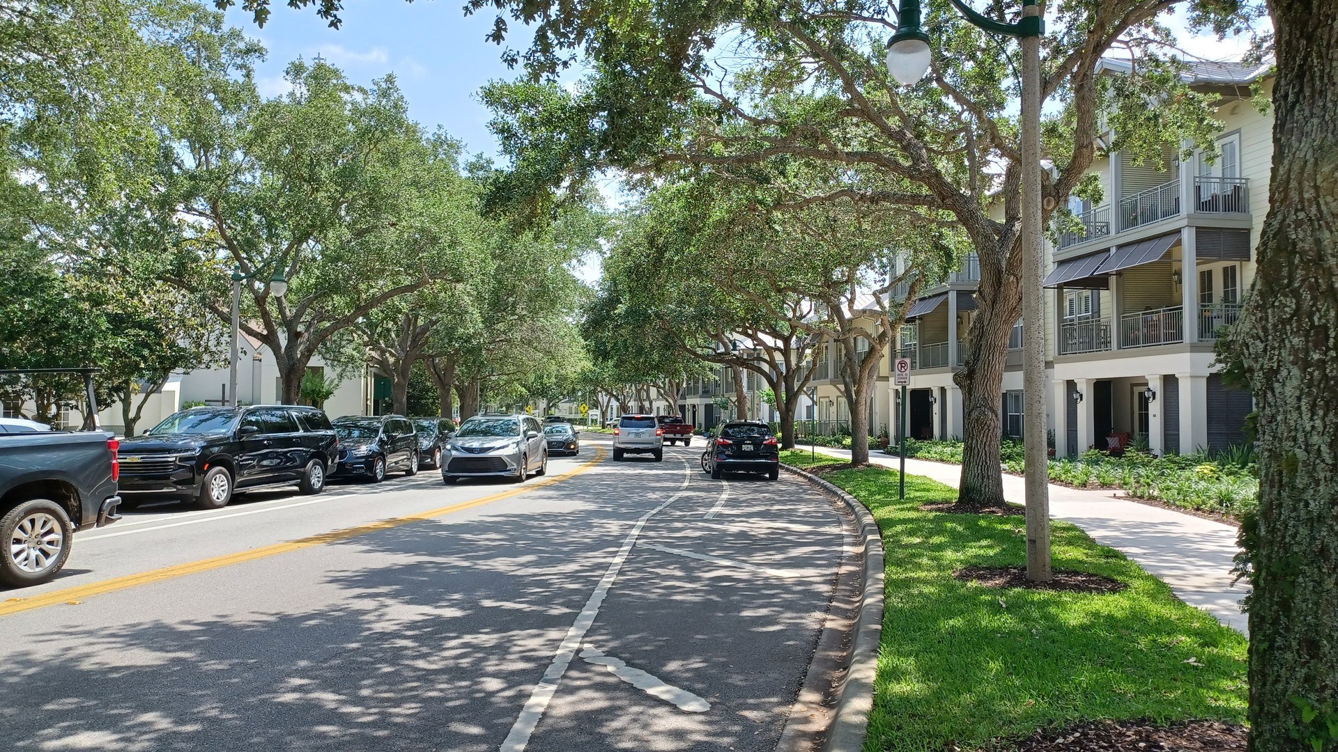Fileira de sobrados iguais com varandas, à sombra de carvalhos, numa avenida residencial de Celebration, na região de Orlando, com carros estacionados na rua