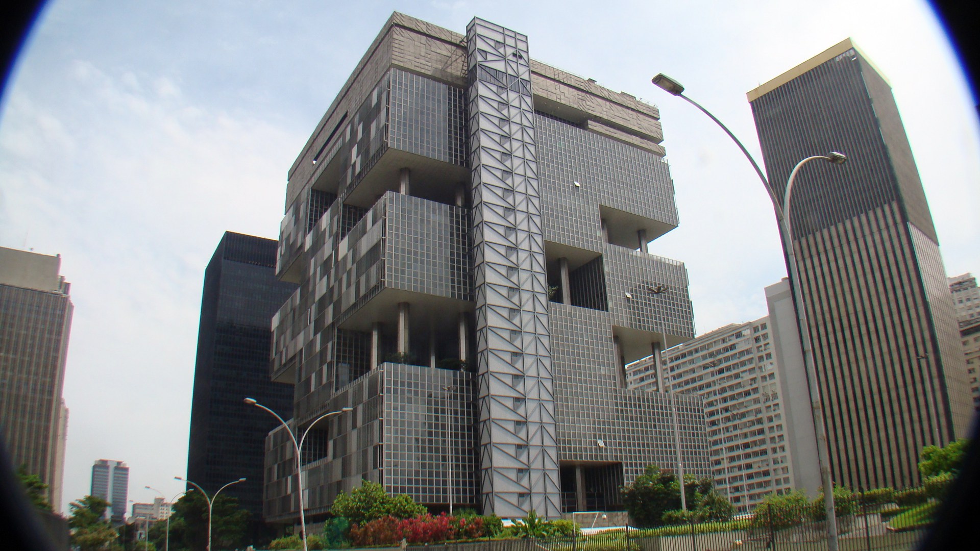 Edifício-sede da Petrobras no centro do Rio de Janeiro, prédio de concreto e vidro com terraços vazados, visto de baixo entre torres de escritório e postes de luz