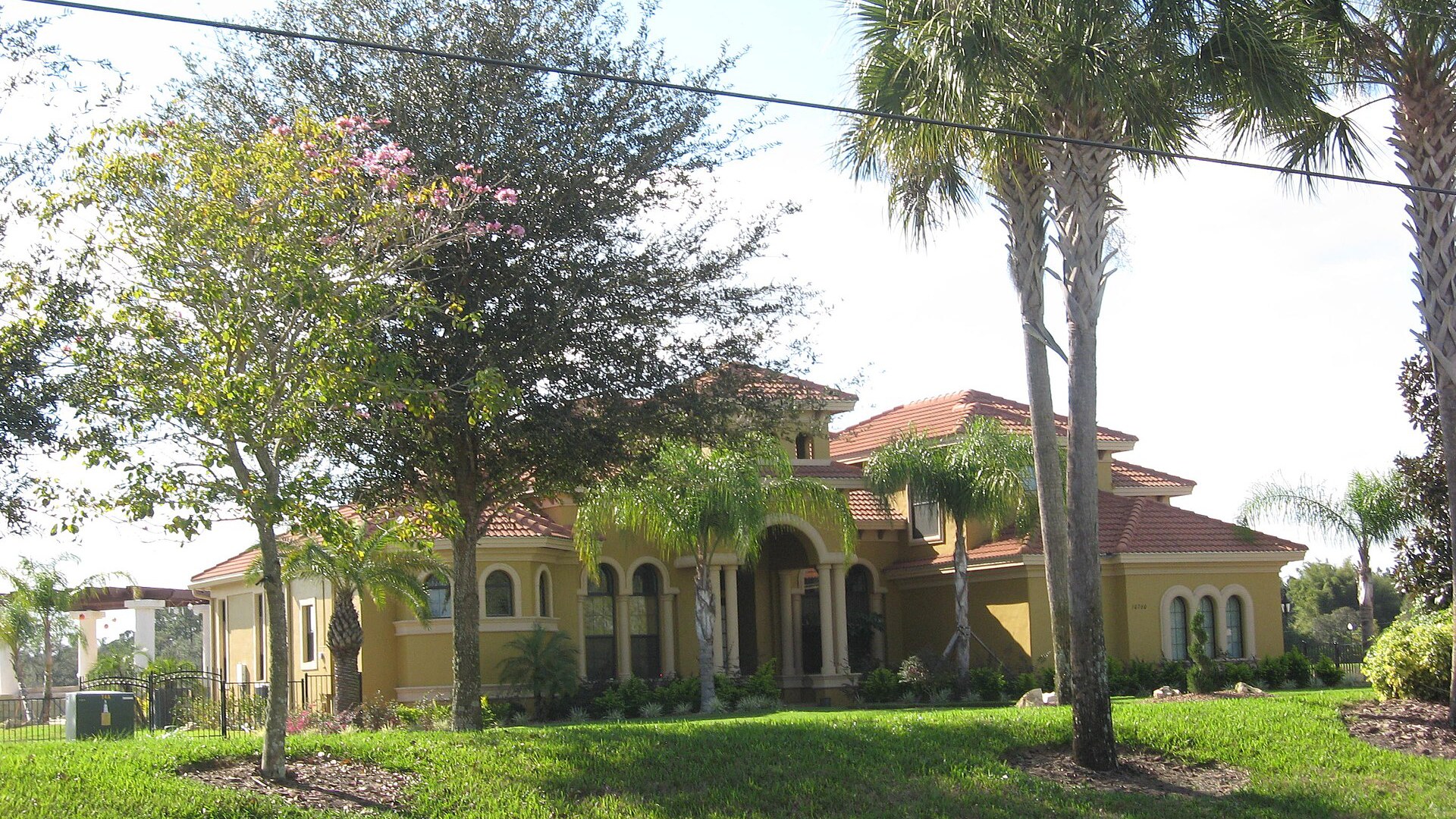 Casa térrea e de dois andares em estilo mediterrâneo, com telhado de telhas cerâmicas, fachada amarela com janelas em arco, gramado, jardim e palmeiras, no sudeste de Orlando