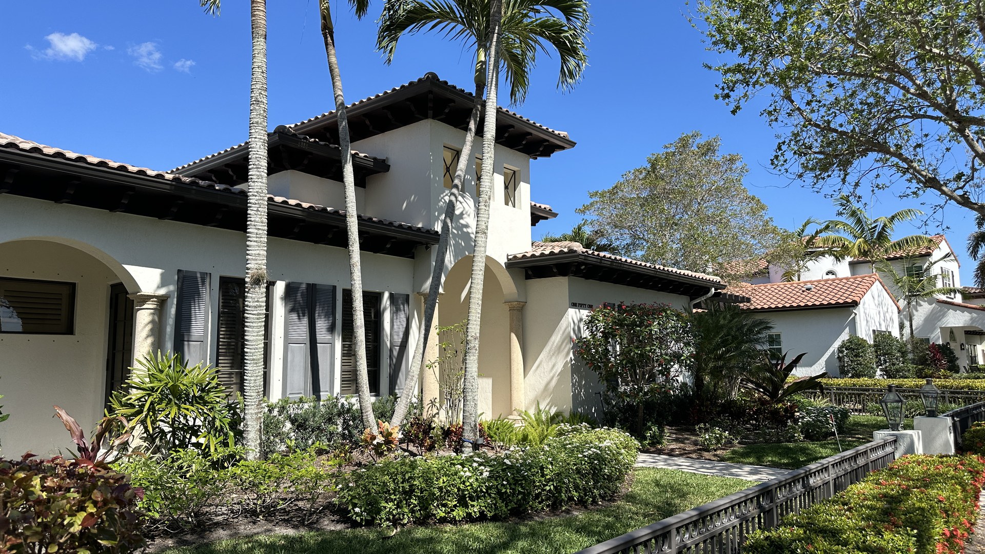 Casa de estilo mediterrâneo, de paredes brancas e telhado de telha, com palmeiras e jardim tropical na frente, no bairro Abacoa, em Jupiter, na região de West Palm Beach